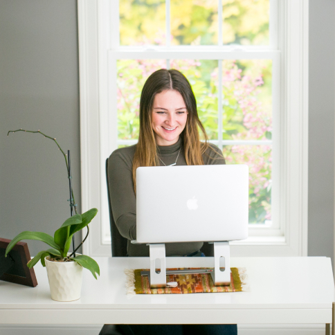Brunette woman sitting in a home office with a laptop open in front of her.