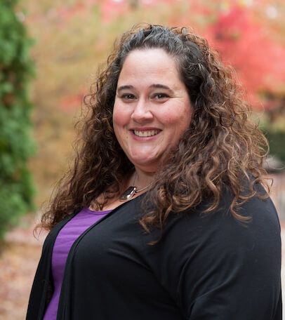Livian-Meet The Team Rebecca Shanahan, a brunette woman with curly hair, smiling and standing outside.